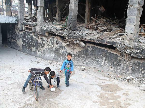 Spielende Kinder neben einem zerstörten Haus in einer Straße in einem Vorort von Damaskus.