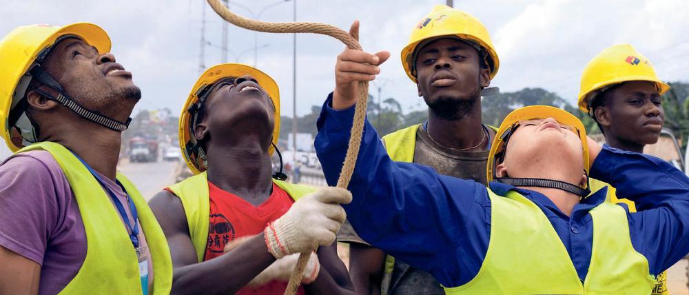 Hierarchien an der Elfenbeinküste. Ein chinesischer Ingenieur von PowerChina and Sinohydro, umringt von seinen einheimischen Mitarbeitern von Ci-Energies beim Bau einer Hochspannungsleitung im Distrikt Yopougon in Abidjan (2015).