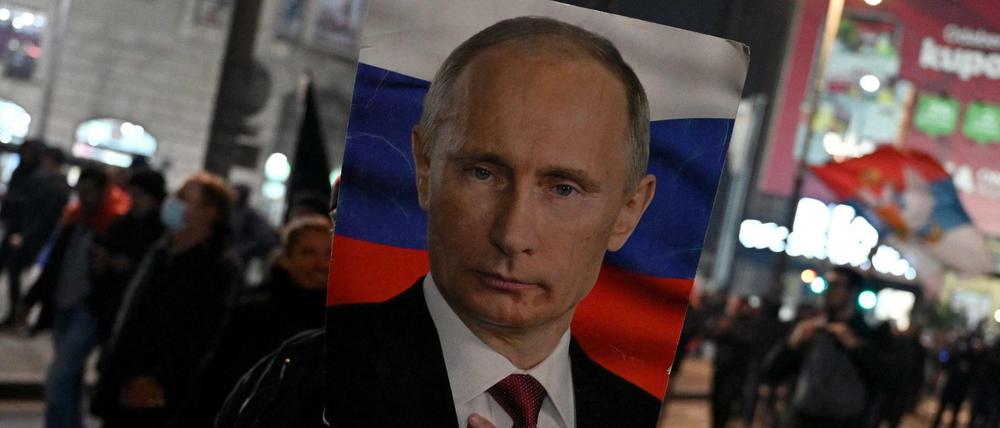 Bei einer Demonstration in Belgrad wird ein Plakat mit einem Foto des russischen Präsidenten vor ein Gesicht gehalten.