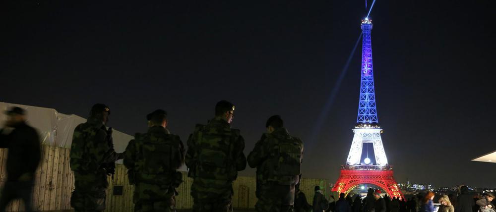Zum Gedenken leuchtet der Eiffelturm am Montagabend in Bleu-blanc-rouge, davor patrouillieren Soldaten zur Terrorabwehr.