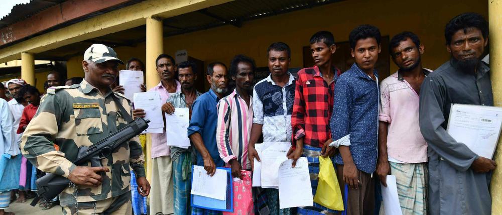 Unter den Augen eines bewaffneten Wachmanns stehen Menschen im nordindischen Bundesstaat Assam Schlange, um nachzuschauen, ob ihre Namen im neuen Bürgerregister stehen.