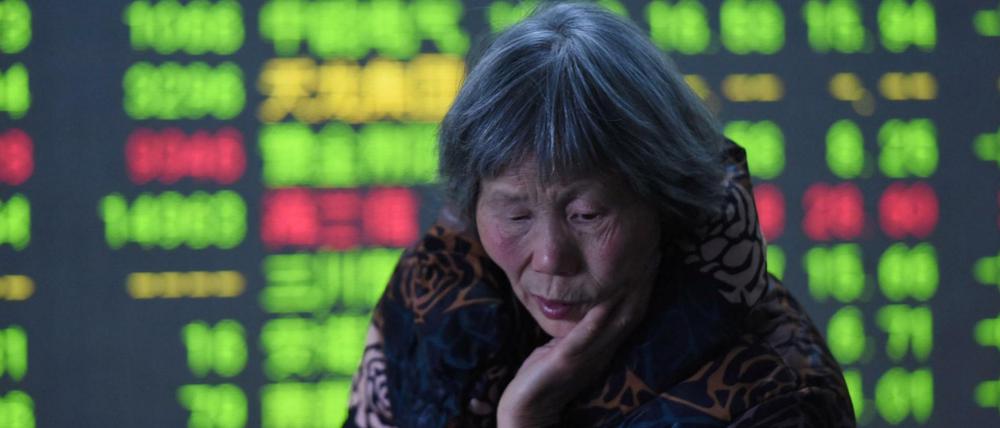 Eine ältere Chinesin steht in Hangzhou in der Provinz Zhejiang vor den aktuellen Börsenkursen. In China sind sinkende Kurse grün gefärbt. 