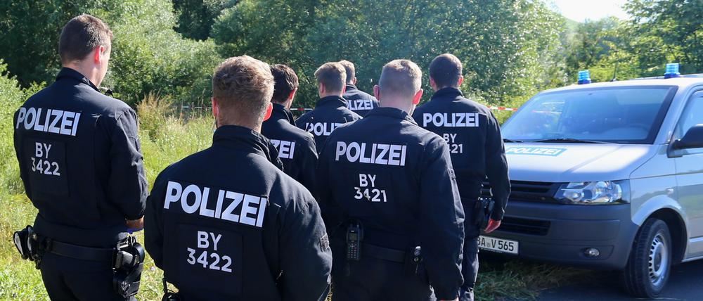 Polizisten durchsuchen am Morgen nach dem Axt-Angriff eines Afghanen das Gelände neben einem Weg bei Würzburg nach Spuren. 