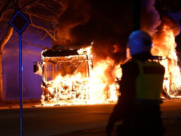 Bereitschaftspolizisten in Malmö (Schweden) beobachten einen brennenden Stadtbus.