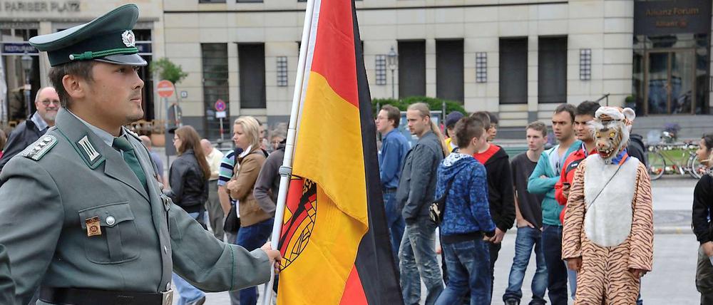 Mann mit DDR-Uniform und Fahne am Brandenburger Tor.