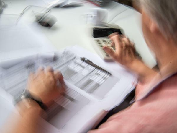 Ein Rentner füllt seine Steuererklärung aus und tippt zur Berechnung Zahlen in einen Tischrechner