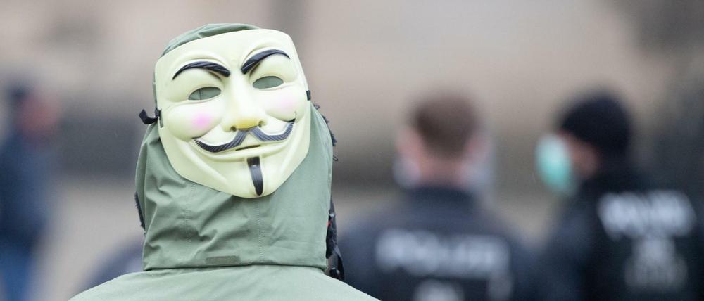 Eine Frau mit einer Guy-Fawkes-Maske steht hinter Polizisten. Zuvor hatten die sogenannten "Corona-Rebellen" im Internet zu einer Demonstration aufgerufen.