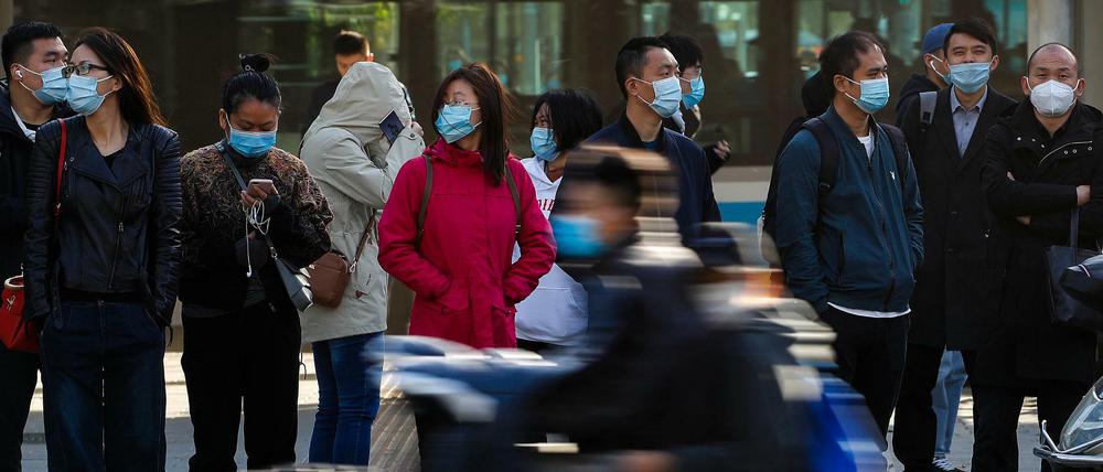Menschen in China tragen Schutzmasken und warten während des morgendlichen Berufsverkehrs darauf, eine Straße zu überqueren. (Symbolbild)