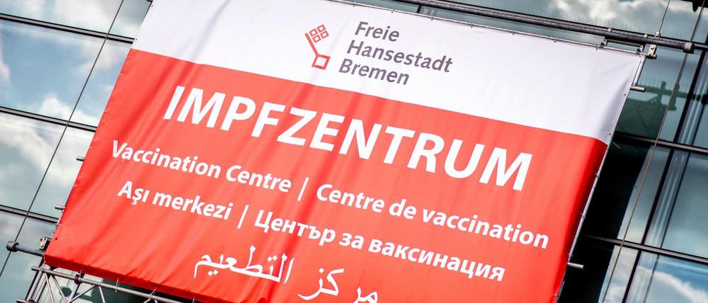 Ein Schild mit der Aufschrift ·Impfzentrum· in mehreren Sprachen hängt über dem Eingang des Impfzentrums in der Messehalle in Bremen.