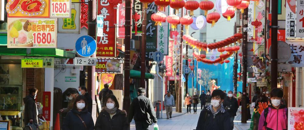 Passanten tragen Schutzmasken und gehen durch China Town von Yokohama, Japan.