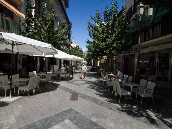 Passanten gehen an fast menschenleeren Tischen und Stühlen vor Restaurants und Bars im spanischen Benidorm entlang.