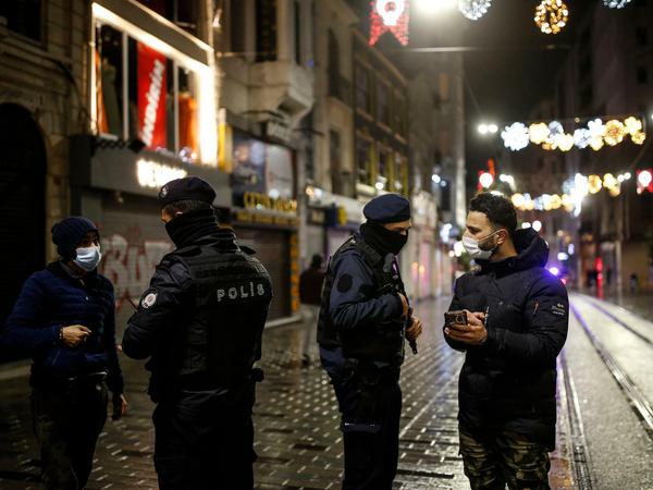 Polizisten sprechen mit Menschen, die sich wenige Minuten nach Beginn der Sperrstunde auf der Istiklal-Straße, der Haupteinkaufsstraße in Istanbul, befinden. 