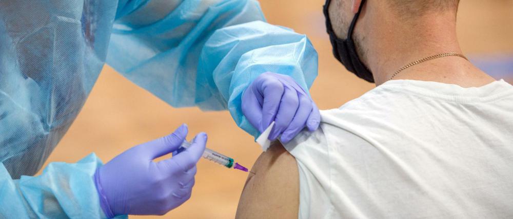 Eine Mitarbeiterin des Gesundheitswesens injiziert einem Mann in einem Impfzentrum einen Corona-Impfstoff. 