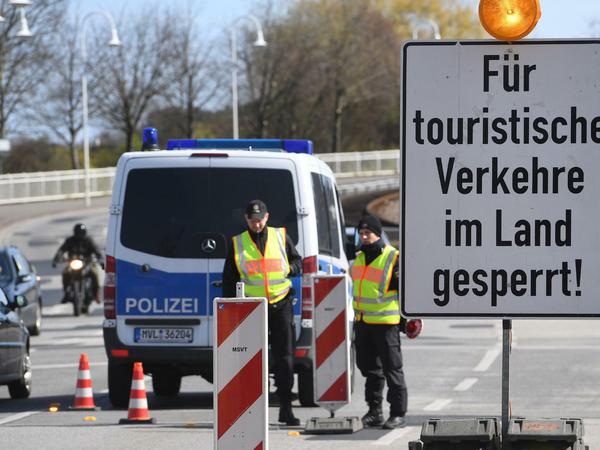 Polizeibeamte kontrollieren hinter einem Schild mit der Aufschrift "Für touristische Verkehre im Land gesperrt!" die Zufahrt zur Insel Usedom. 