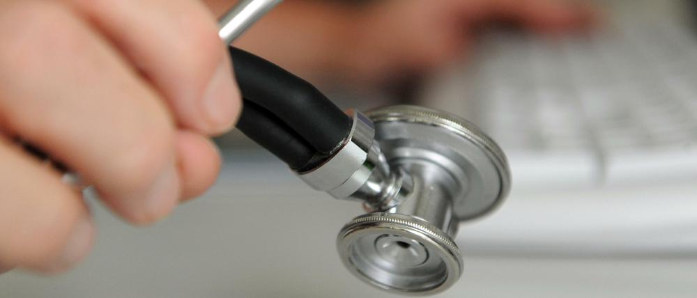 Ein Arzt hält in einem Behandlungszimmer in seiner Praxis ein Stethoskop in der Hand.