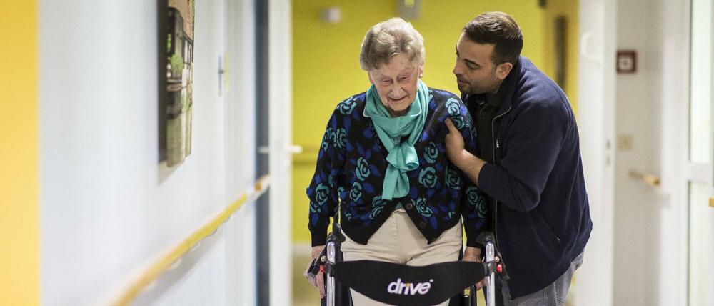 Eine Frage der Zuwendung: Ein Therapeut begleitet eine Seniorin am Rollator.