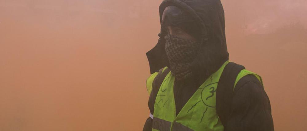 Ein vermummter Demonstrant der sogenannten "Gelbwesten" steht in dichtem Rauch von Rauchgranaten. 