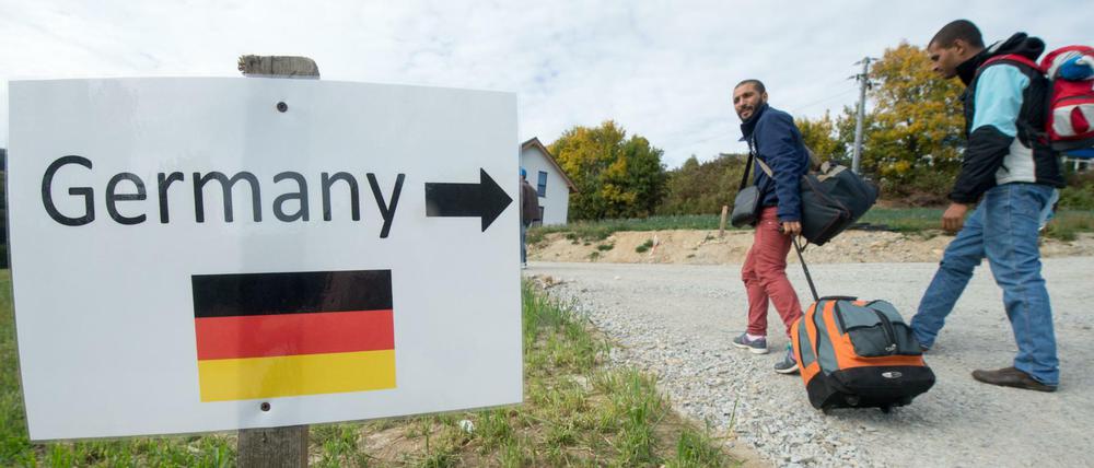 Flüchtlinge aus Syrien gehen am 06.10.2015 im österreichischen Julbach nahe der deutschen Grenze an einem Schild mit der Aufschrift "Germany" und der Abbildung einer deutschen Flagge vorbei. 