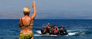 Ein Badegast winkt Flüchtlingen aus Syrien zu, die aus der Türkei mit einem Schlauchboot an die Küste von Mitilini auf der Insel Lesbos kommen. 