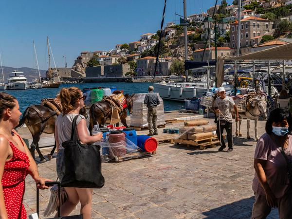 Touristen und Einheimische mit Maultieren stehen am Hafen der Insel Hydra, 65 Kilometer südwestlich von Athen entfernt. 