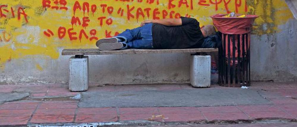 Griechische Tristesse. Ein Mann schläft im Hafenviertel von Piräus auf einer Bank. 