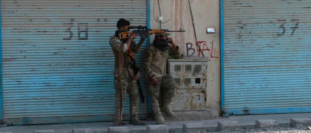 Zwei bewaffnete afghanische Sicherheitskräfte stehen auf einer Straße, auf der Patronenhülsen liegen und kämpfen mit Taliban.