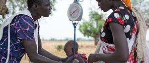 Ein Mitarbeiter einer Hilfsorganisation wiegt im Südsudan ein Kind.