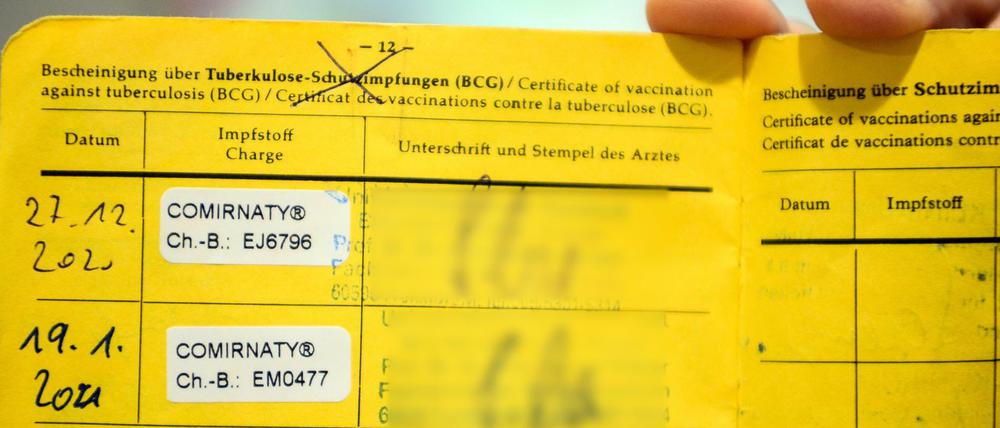 -Eine Person hält einen gelben Impfpass mit den Aufklebern vom Biontech-Pfizer-Impfstoff.