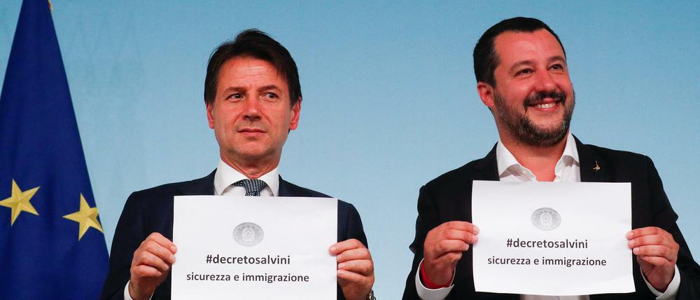 Ministerpräsident Giuseppe Conte und Innenminister Matteo Salvini halten Papiere mit dem Titel des Dekrets über den Umgang mit Migranten hoch.