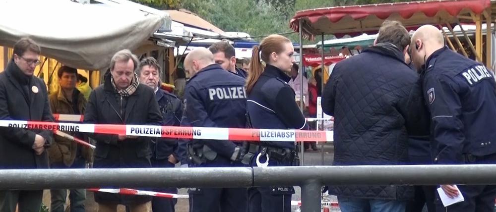 Polizeibeamte stehen am 17.10.2015 in Köln am Tatort am Braunsfelder Wochenmarkt. Die Kölner Oberbürgermeisterkandidatin Henriette Reker ist einen Tag vor der Wahl bei einer Messerattacke in Köln verletzt worden. 