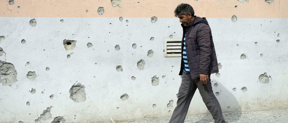 Ein Mann geht an einer Hauswand in Aserbeidschan vorbei, an der viele Einschusslöcher zu sehen sind.