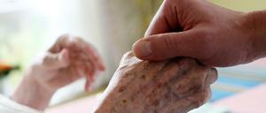 Ein Pfleger hält in einem Alten-und Pflegeheim die Hand einer Bewohnerin