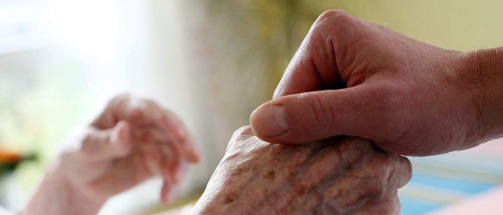 Ein Pfleger hält die Hand einer Bewohnerin eines Pflegeheims. 