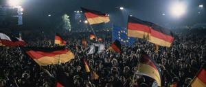 Menschen feiern die Deutsche Wiedervereinigung, dabei schwenken sie deutsche Flaggen und Fahnen. Aufgenommen in Berlin am 03.10.1990.