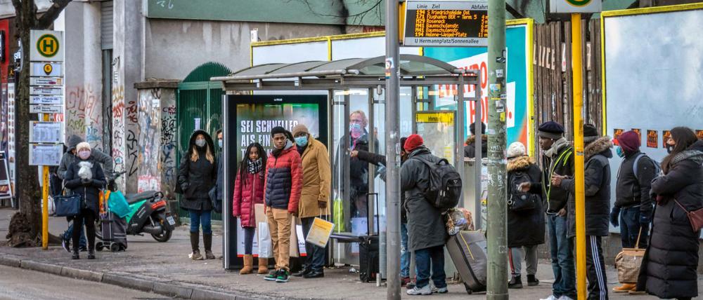 Menschen an einer Bushaltestelle beim Hermannplatz in Neukölln. 
