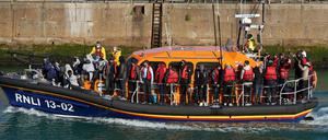 Eine Gruppe von Menschen, vermutlich Migranten, tragen Schwimmwesten, während sie auf einem Rettungsbot mit einem kleinen Boot im Ärmelkanal nach Dover gebracht werden. 