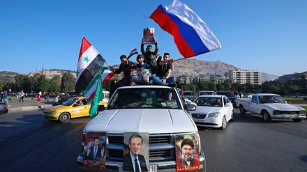 Unterstützer der syrischen Regierung in Damaskus schwenken eine syrische, eine russische und eine iranische Fahne.