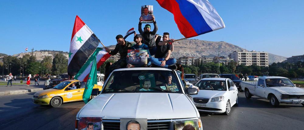 Unterstützer der syrischen Regierung in Damaskus schwenken eine syrische, eine russische und eine iranische Fahne.