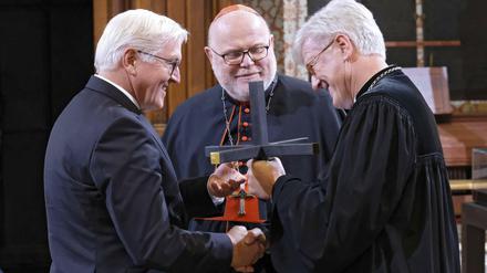 Landesbischof Bedford-Strohm (r.) und Kardinal Marx überreichen ein Kreuz an Bundespräsident Steinmeier (l.)