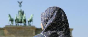 Eine muslimische Frau mit Kopftuch steht vor dem Brandenburger Tor in Berlin.
