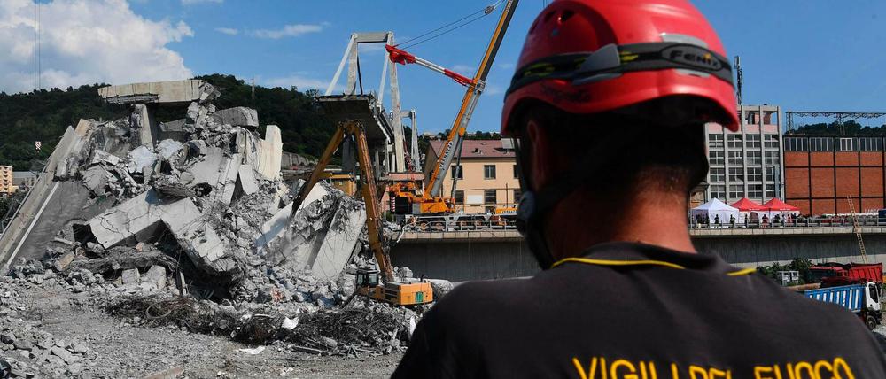 Ein Feuerwehrmann schaut auf Bagger, die Trümmer der teilweise eingestürzten Morandi-Autobahnbrücke entfernen.