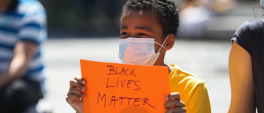 Ein Junge mit Mundschutz hält während einer Demonstration ein Plakat mit der Aufschrift «Black lives matter» in der Hand.