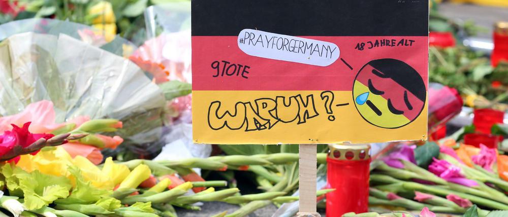 Ein Aufsteller in den deutschen Nationalfarben mit der Aufschrift "#prayforgermany" und "Warum?" steht vor dem Olympia-Einkaufszentrum in München, einen Tag nach einer Schießerei mit Toten und Verletzten, inmitten von Blumen zum Gedenken an die Opfer. Die tödlichen Schüsse hat ein 18-jähriger Deutsch-Iraner abgegeben. 
