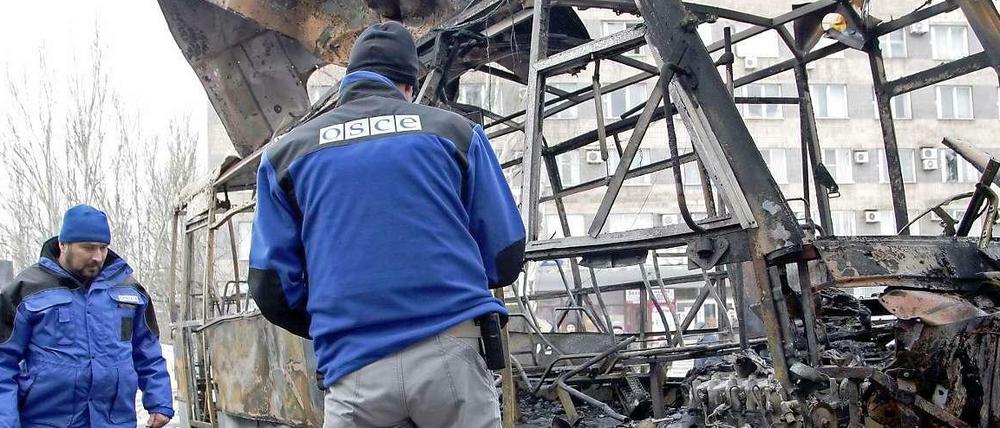 Beobachter der OSZE betrachten einen vollkommen zerstörten Bus an einem Busbahnhof im ostukrainischen Donezk.