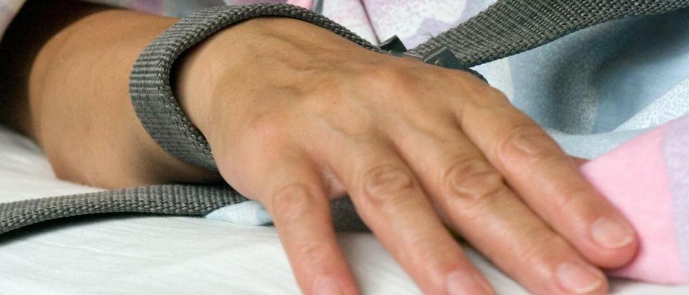 Eine mit einem Textilband festgebundene Hand eines Patienten.