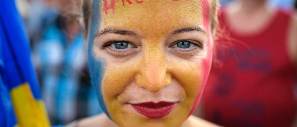 Eine Frau hat ihr Gesicht in den rumänischen Nationalfarben geschminkt, auf ihrer Stirn steht der Hashtag #Widerstand. 
