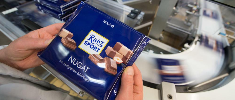 Eine Mitarbeiterin des Schokoladenherstellers Ritter Sport prüft die Verpackung einer Tafel Schokolade. 