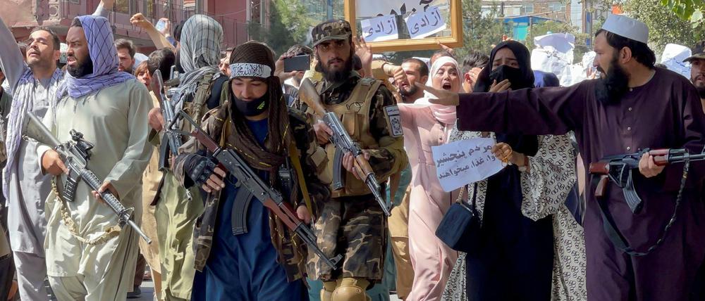Demonstranten laufen hinter den Taliban-Kämpfern.