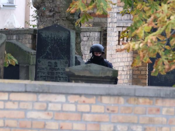 Ein Polizist mit Schutzhelmen steht zwischen Grabsteinen auf dem jüdischen Friedhof in Halle. 