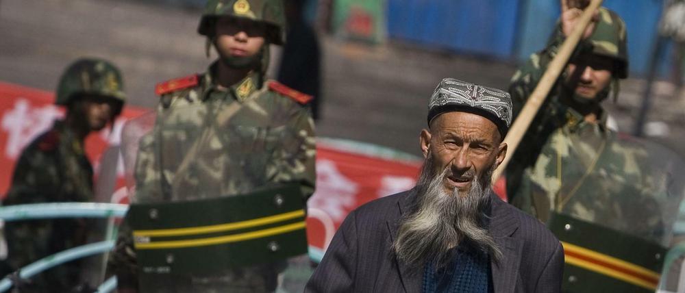 Ein Angehöriger der uigurischen Minderheit geht in der Unruheregion Xinjiang an chinesischen Sicherheitskräften vorbei.